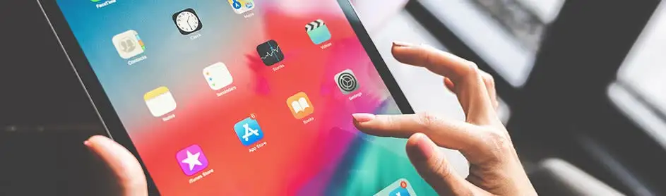 Une tablette affiche des icônes d'applications sur un écran aux couleurs vives, touchée par un doigt.