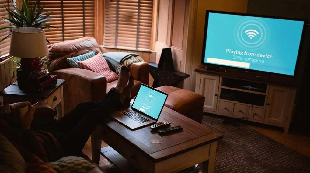 Living room with a laptop on a wood table, a sofa, and a TV playing from device. The screen shows 52% complete.