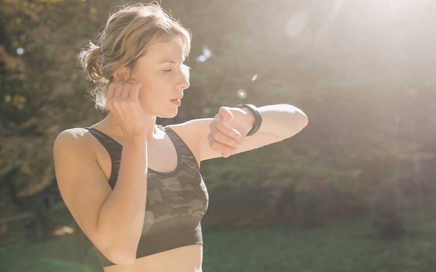 Een persoon in een camouflage sportbeha kijkt naar een zwarte smartwatch buiten in het park.