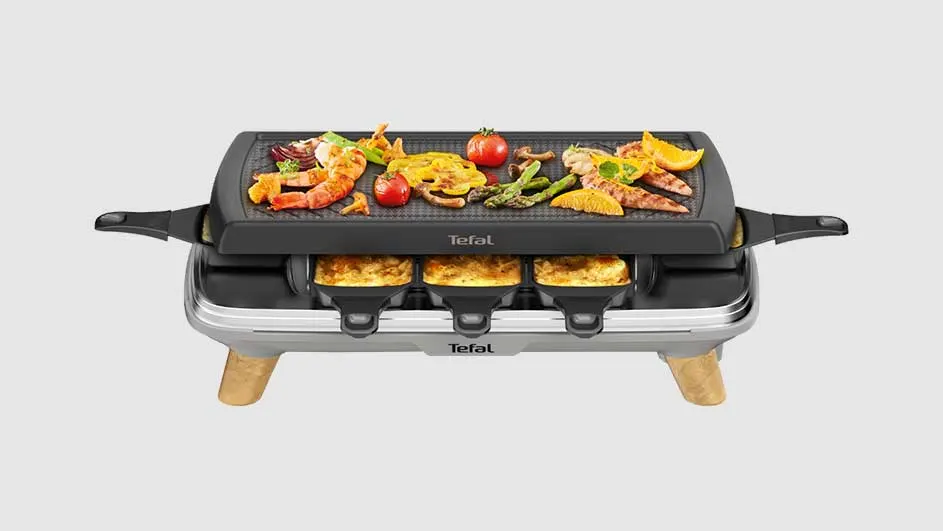 Gril de table noir et argenté avec crevettes, légumes et tomates. Trois poêlons sont visibles en dessous.