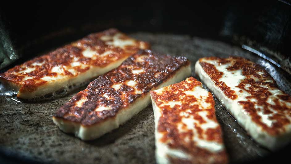 Quatre tranches de halloumi dorées dans une poêle. Le fromage est blanc avec des taches dorées.