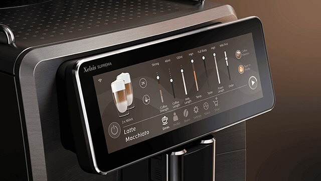 Zwarte koffiemachine met touchscreen dat een latte macchiato-optie toont en instelbare balken voor koffie- en melkvolume.