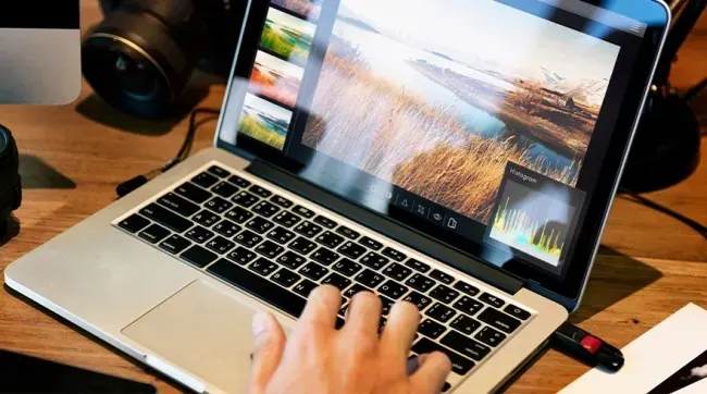 Un ordinateur portable affiche une photo retouchée. Une caméra noire est à gauche, sur une table en bois. Une clé USB est branchée.