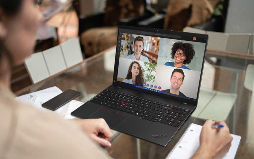 Une personne participe à une visioconférence sur un ordinateur ThinkPad, avec quatre participants visibles et des notes près de l’appareil.