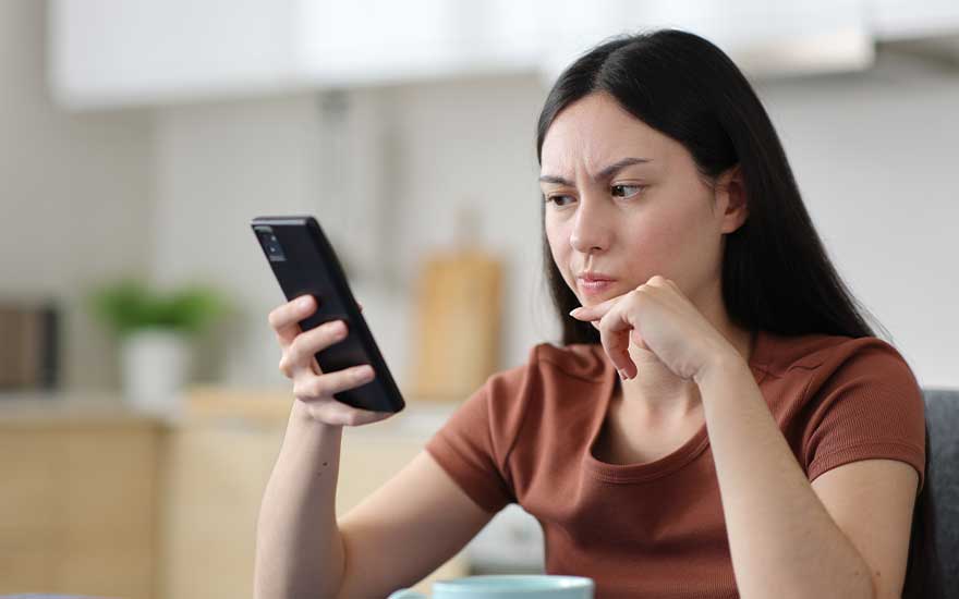 Une femme regarde son smartphone avec inquiétude dans la cuisine, comme si elle lisait une alerte ou un problème.