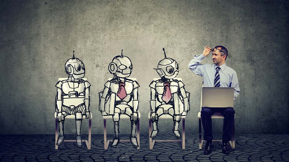 Een man met een laptop zit naast getekende robots tegen een grijze achtergrond.