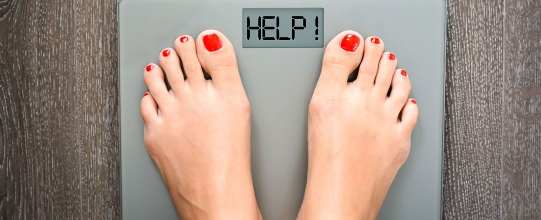 Deux pieds avec du vernis rouge sur une balance grise affichant "HELP !" sur un sol en bois.