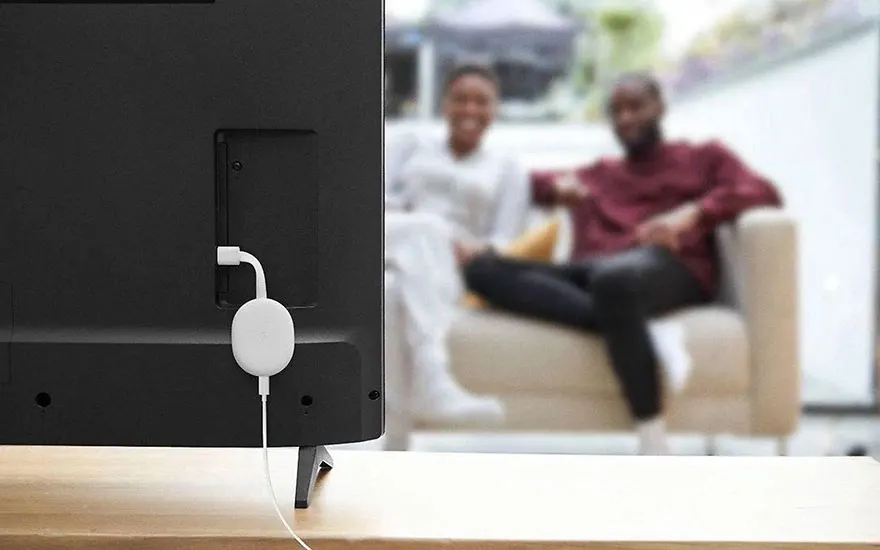 Een zwarte tv met een witte streaming dongle aangesloten. Op de achtergrond een lichte zetel.