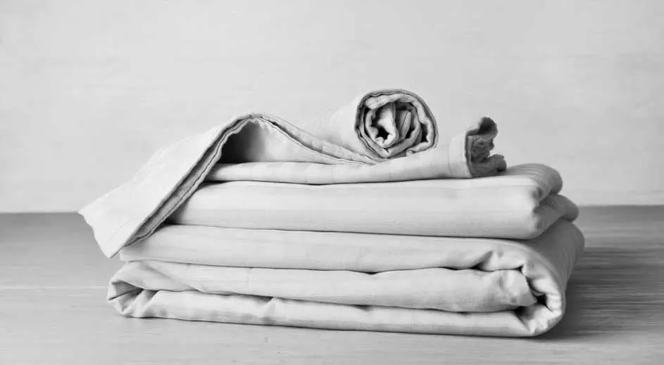 Gros plan sur une pile de draps gris pliés sur une table en bois devant un mur gris clair.