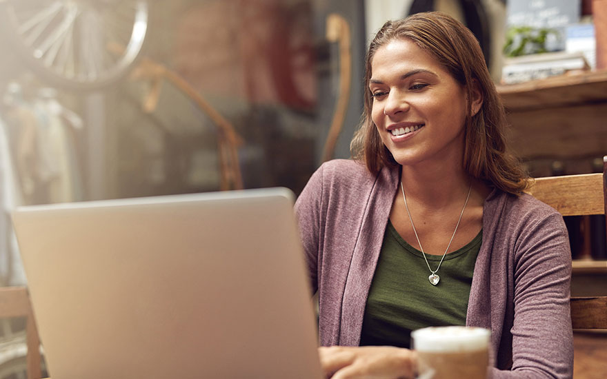 Een laptop staat op een tafel met een drankje. Op de achtergrond is er een decoratief fietswiel.