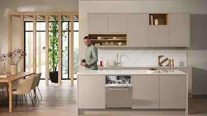 Dans une grande cuisine lumineuse, un lave-vaisselle encastré dans l’îlot central est ouvert et rempli de vaisselle, ambiance conviviale.