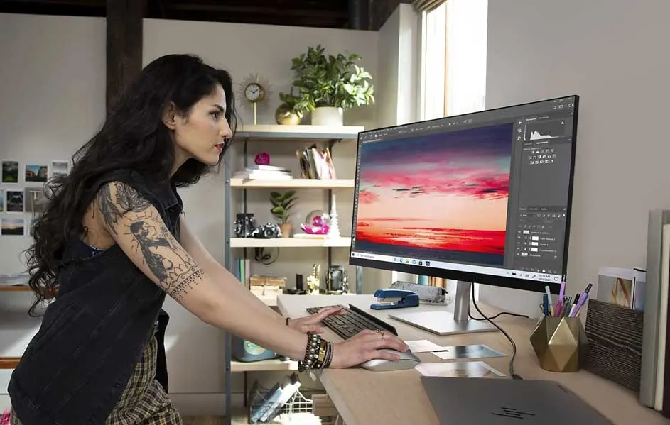 Bureau avec ordinateur affichant un ciel rougeoyant. Étagère avec plante et décorations en arrière-plan. Clavier et souris sur le bureau.
