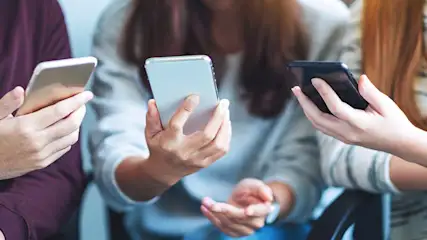 Trois personnes tiennent des smartphones. Les écrans sont allumés. Les appareils sont argentés et noirs.