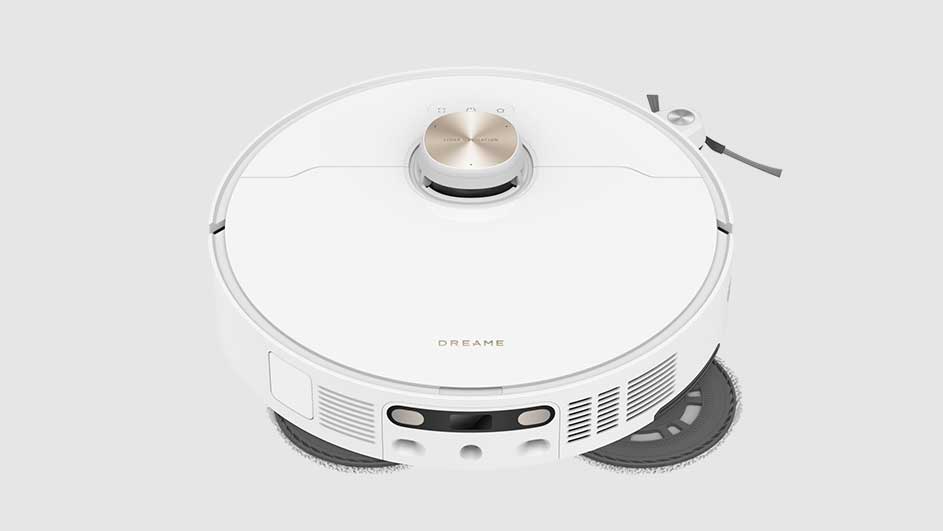 Un aspirateur robot blanc sur fond blanc. L'appareil est rond avec un bouton doré sur le dessus et une brosse sur le côté.