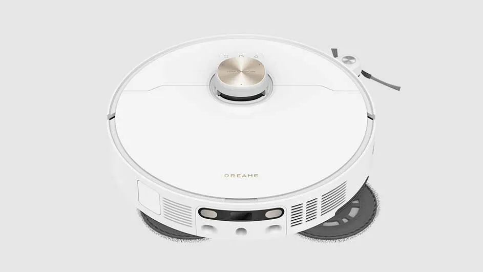 Un aspirateur robot blanc sur fond blanc. L'appareil est rond avec un bouton doré sur le dessus et une brosse sur le côté.