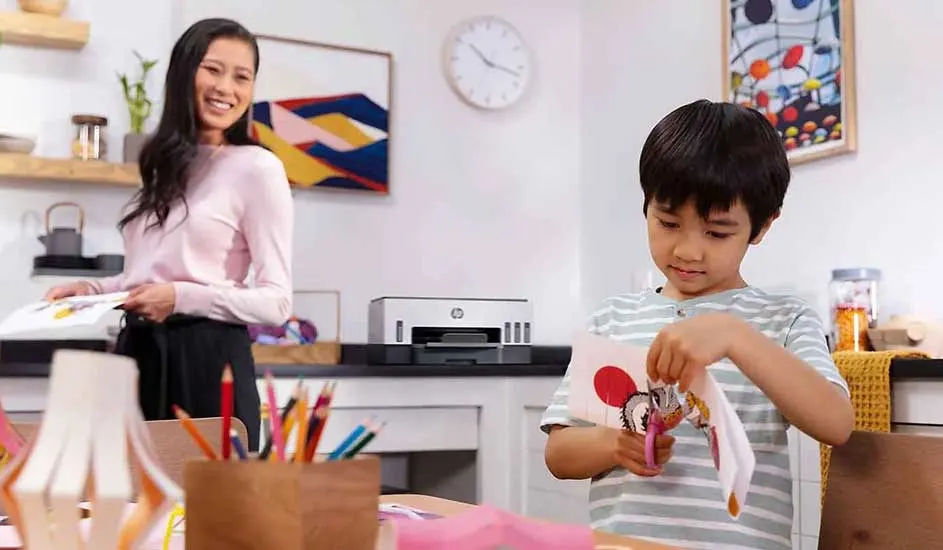 Intérieur lumineux avec bureau où un enfant découpe du papier avec des ciseaux. Une imprimante blanche est visible sur une étagère.