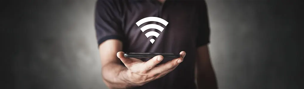 Un téléphone noir est tenu devant un symbole Wi-Fi blanc, sur un fond gris foncé.