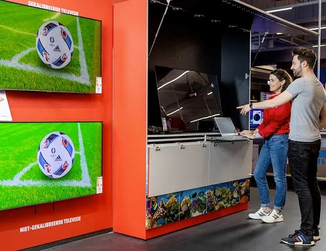 Deux écrans affichent un ballon de foot sur un terrain vert. Un ordinateur portable est posé sur un comptoir blanc et rouge.