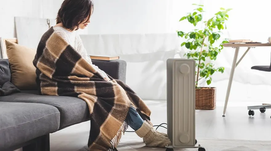 Een grijze sofa met een blokjesdeken, een radiator, en een plant in een mand op een lichte vloer.