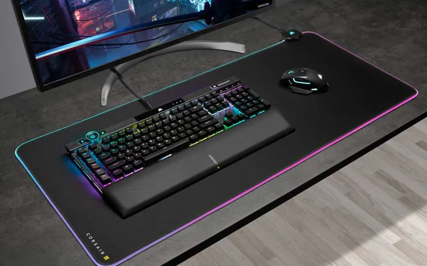Un écran, un clavier rétroéclairé, un repose-poignets, une souris et un tapis de souris lumineux sur un bureau.