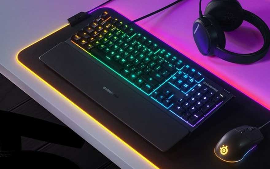 Un clavier rétroéclairé multicolore sur un tapis de souris noir, avec une souris et un casque sur un fond violet.