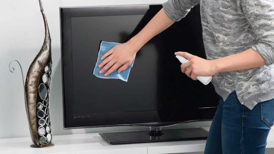 Een zwarte tv wordt schoongemaakt met een blauwe doek en een witte sprayfles. Links staat een decoratieve vaas.