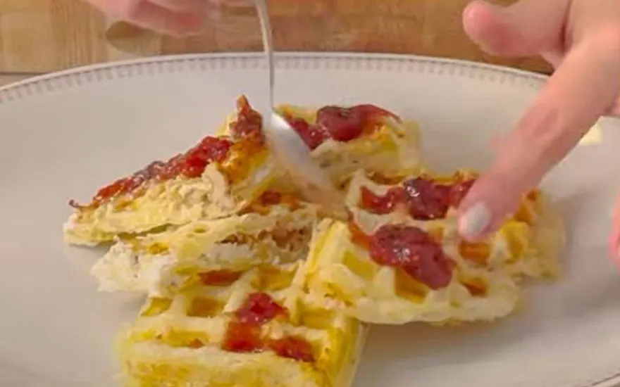 Wafels met rode topping op een wit bord. Een zilveren lepel en een vinger zijn zichtbaar.
