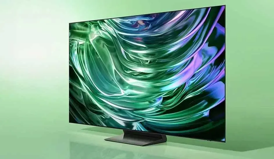 A modern television with an ultra-slim black frame stands on a wide base and displays an abstract pattern of green and purple waves on the screen.