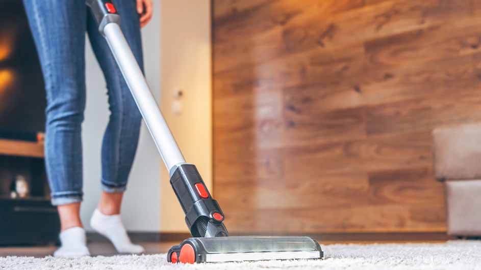 Une personne passe l'aspirateur sur un tapis blanc dans une pièce avec des murs en bois.