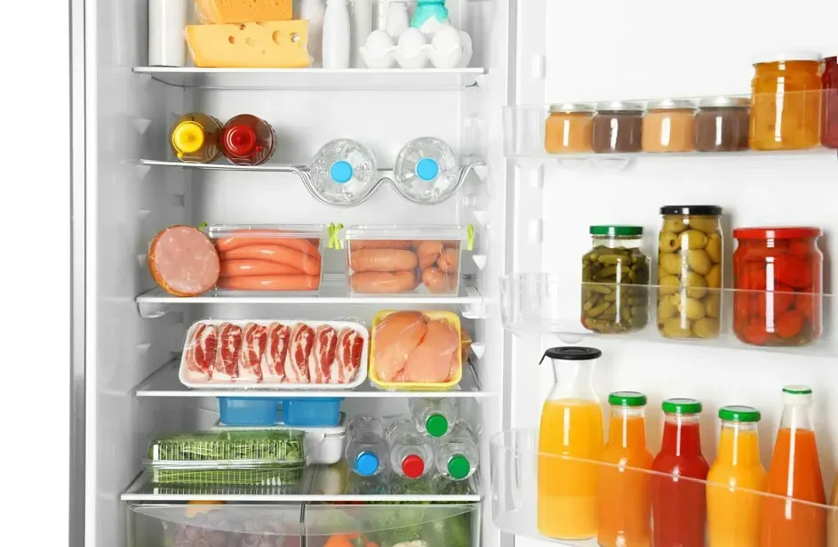 Un réfrigérateur blanc plein de nourriture variée : fromage, conserves, boissons et viande sur plusieurs étagères.