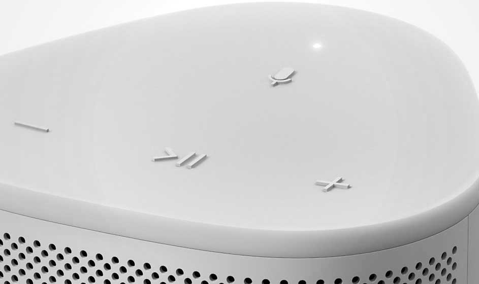 Vue rapprochée d'un haut-parleur blanc avec des boutons tactiles et une grille perforée.