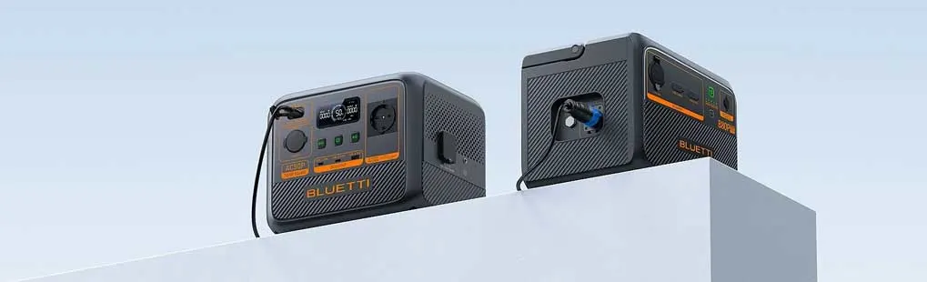 Twee zwarte BLUETTI powerstations met oranje details staan op een witte rand. Ze hebben meerdere aansluitingen en een modern ontwerp.