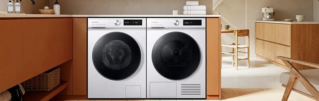 A kitchen features a white washing machine and dryer next to brown cabinets. A table and chair are nearby.