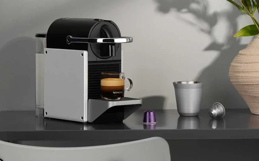 Witte Nespresso Pixie machine op donker oppervlak met verse espresso, paarse capsules en metalen accessoires.