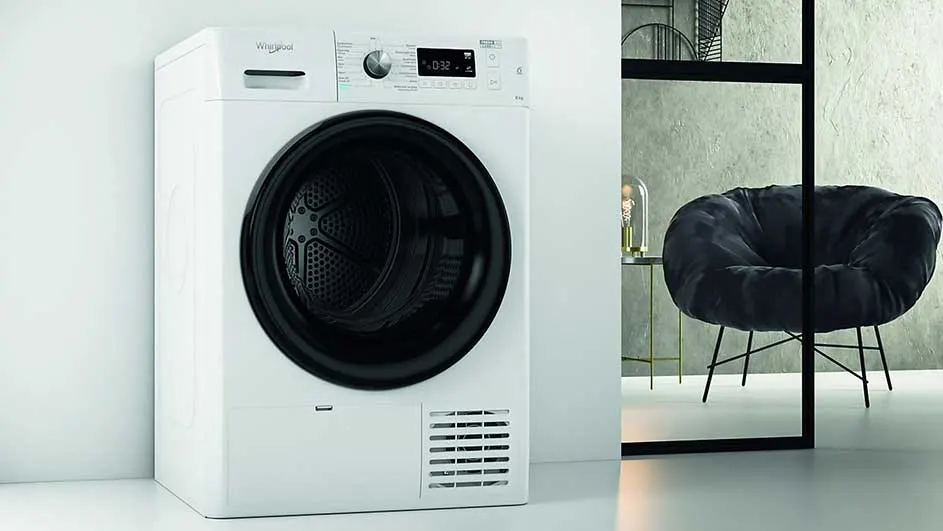 Witte Whirlpool droogkast met zwarte deur, naast een zwarte stoel en een lamp op een goudkleurig tafeltje.
