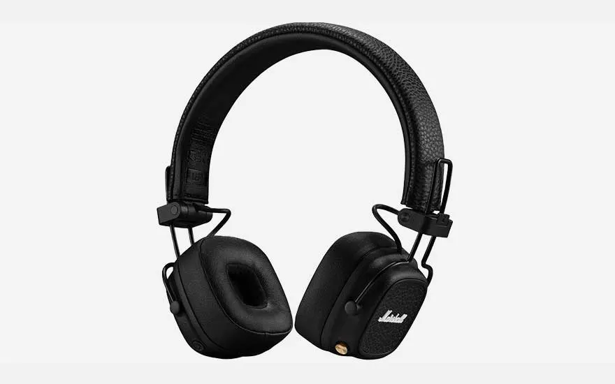 Une personne assise sur une chaise avec un casque écoute de la musique depuis un téléphone sur fond beige.