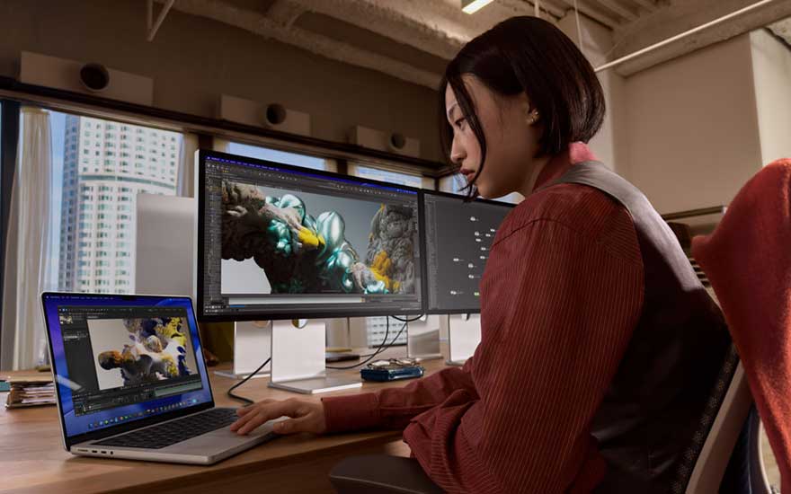 Een ontwerpster werkt met laptop en twee brede monitoren, waarop een kleurrijke digitale illustratie van een vogel wordt bewerkt.