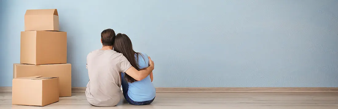 Stapel bruine kartonnen dozen links, tegen een lichtblauwe achtergrond en een houten vloer.
