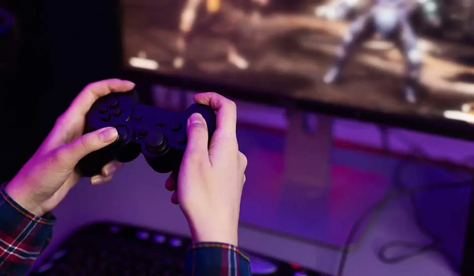 Twee handen houden een zwarte controller vast voor een scherm. Op het scherm is een computerspel te zien. Een toetsenbord is zichtbaar onder het scherm.