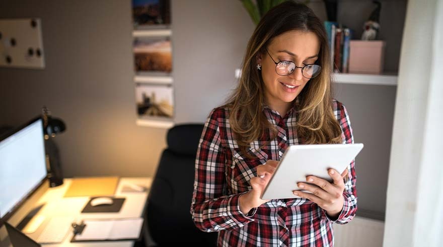 Een tablet wordt gebruikt in een kantoor, met een bureau, computer, bureaustoel, boeken en decoraties op de achtergrond.