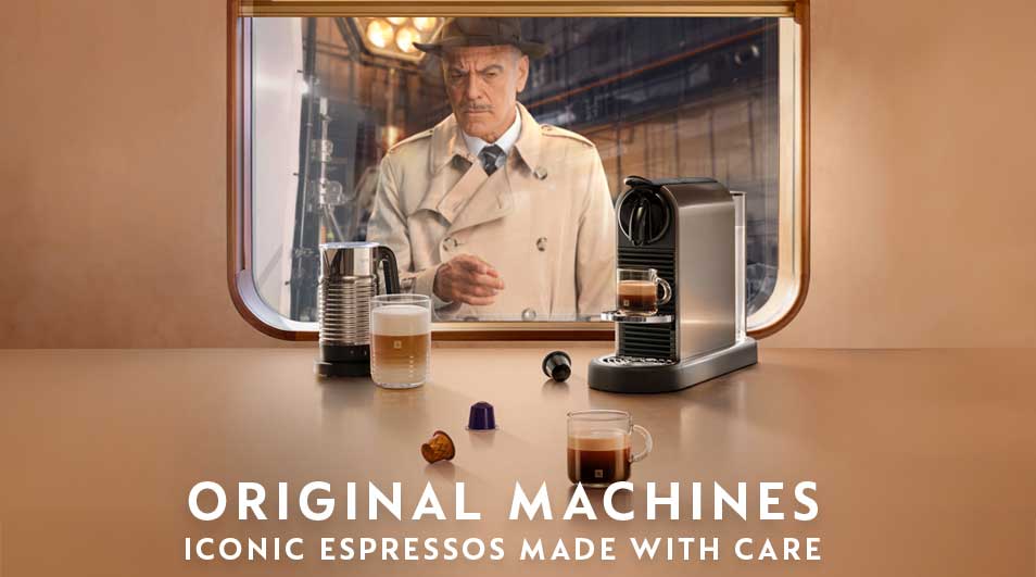 Homme en imperméable beige observe par la fenêtre du train un espresso fumant et des capsules près d’une machine élégante.