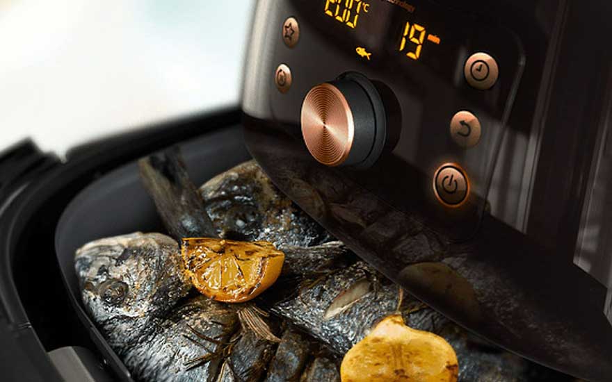 Een zwarte airfryer met goudkleurige details, met daarin gegrilde vis en citroenpartjes. Het display toont een temperatuur van 200 graden.