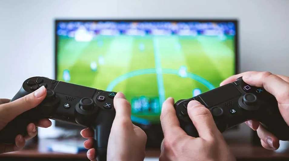 Two hands hold black game controllers in front of a screen showing a green field.