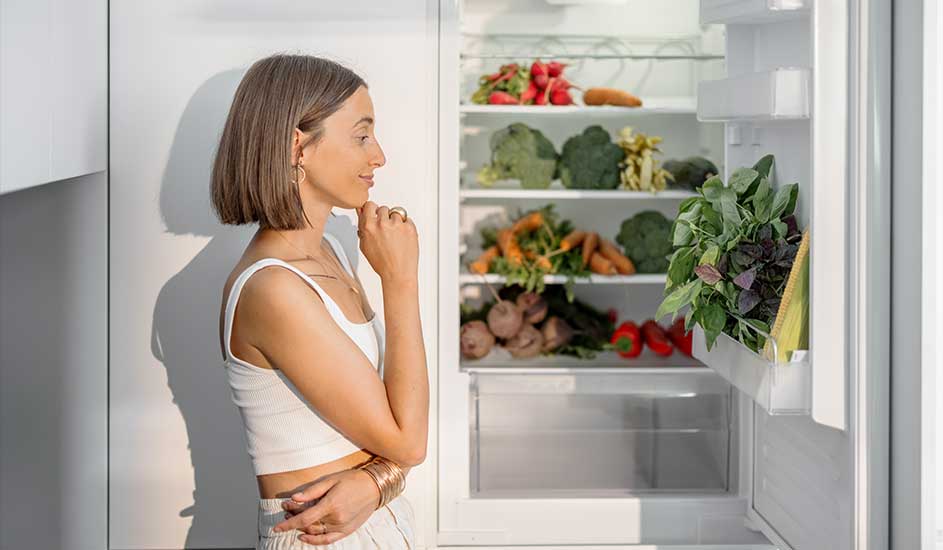 Réfrigérateur blanc ouvert, rempli de légumes colorés comme des carottes, brocolis, radis et herbes fraîches.