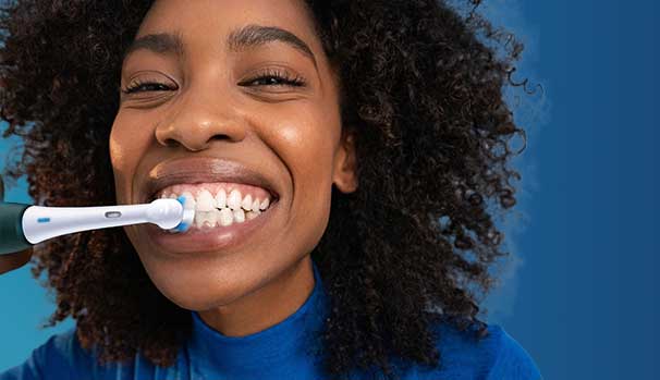 Une femme souriante se brosse les dents avec une brosse à dents électrique; gros plan, cheveux bouclés, fond bleu.