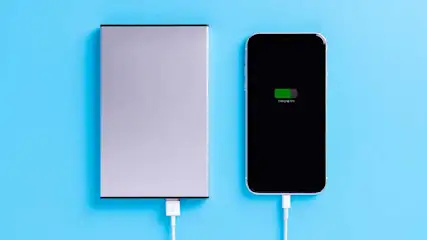Un smartphone et une batterie externe gris sont connectés par un câble blanc sur un fond bleu.