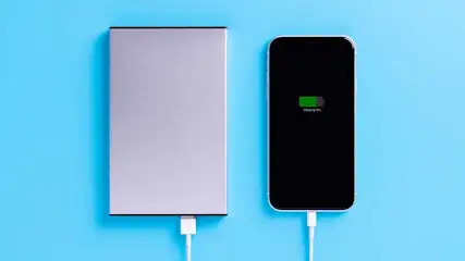Een powerbank en een telefoon zijn met witte kabels verbonden op een blauwe achtergrond. De telefoon laadt op.