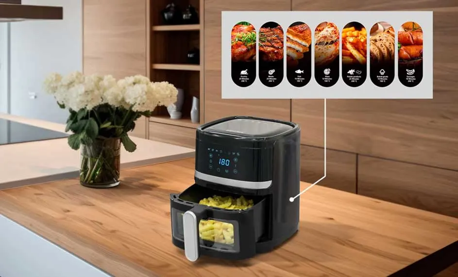 Een zwarte airfryer met frieten staat op een houten aanrecht, met een bloemenvaas en menugids op de achtergrond.