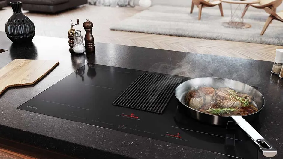 Vue rapprochée d'une plaque de cuisson noire avec une poêle en acier inoxydable contenant de la viande.