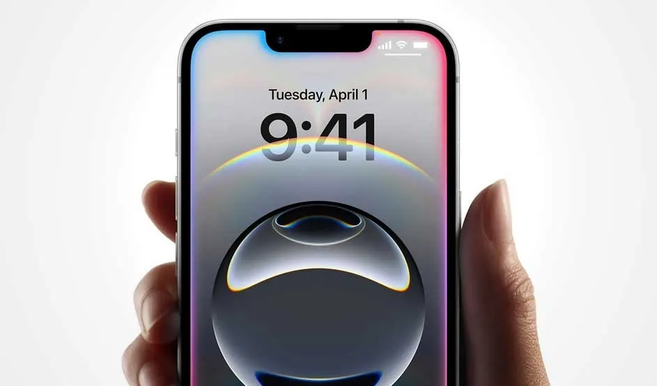 A hand holds an Apple iPhone, showing 9:41 on Tuesday, April 1. Sleek bezels, notch at the top, glossy orb wallpaper, bright, crisp display.